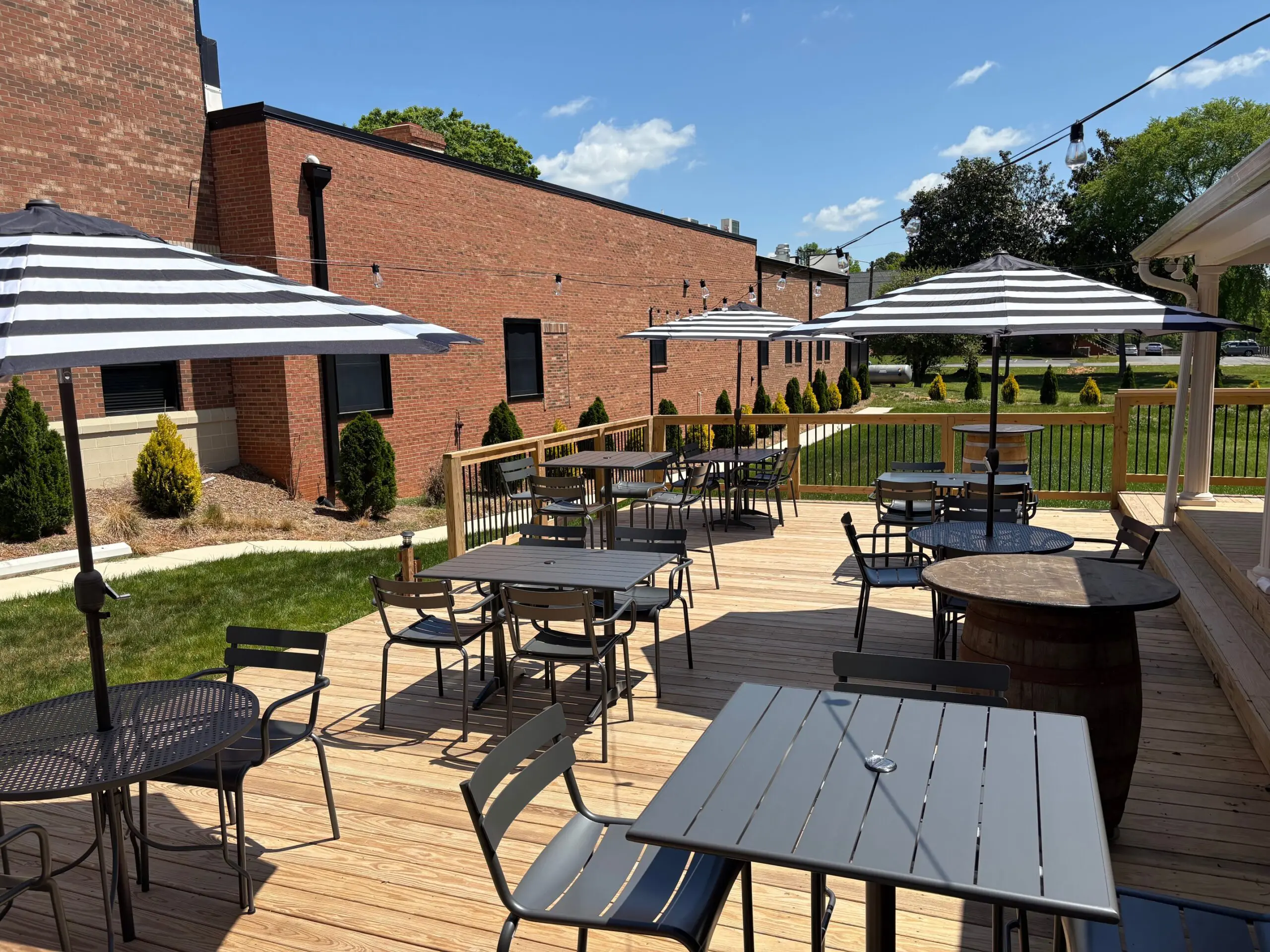 Outdoor patio seating with tables and umbrellas beside a brick building.