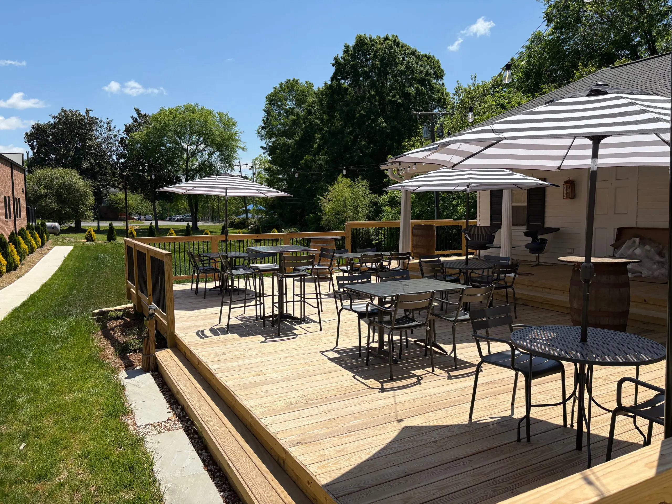 Outdoor wooden deck with tables, chairs, and umbrellas under a sunny sky.