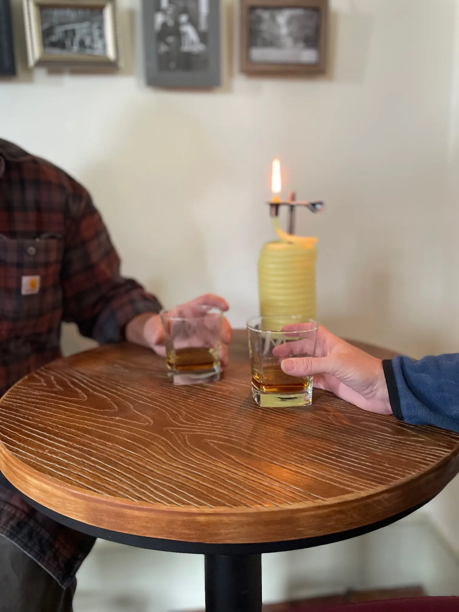 Two people clinking glasses over a wooden table with a lit candle.