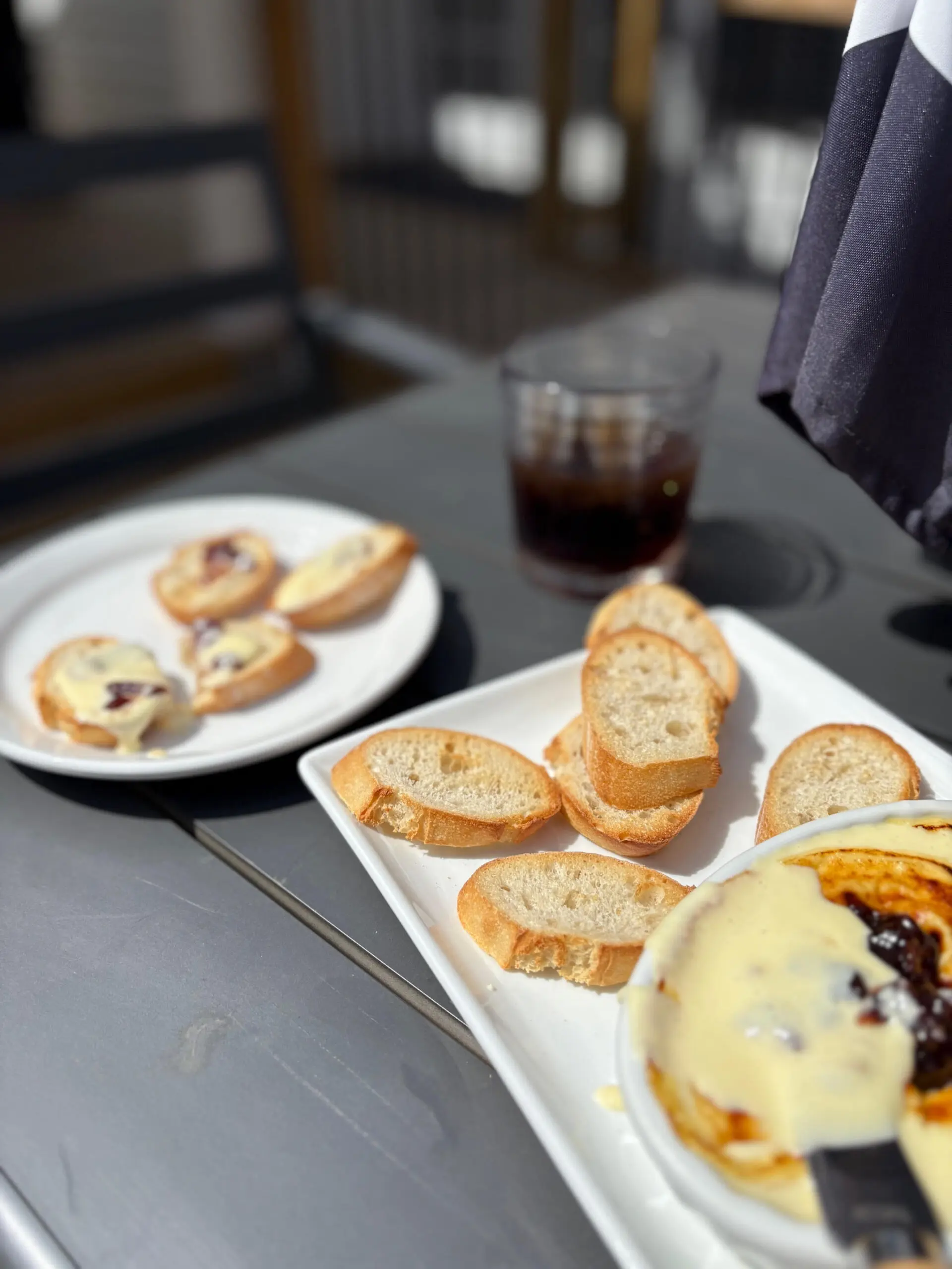 Plates of assorted bread and pastries on a table with a glass of iced drink.