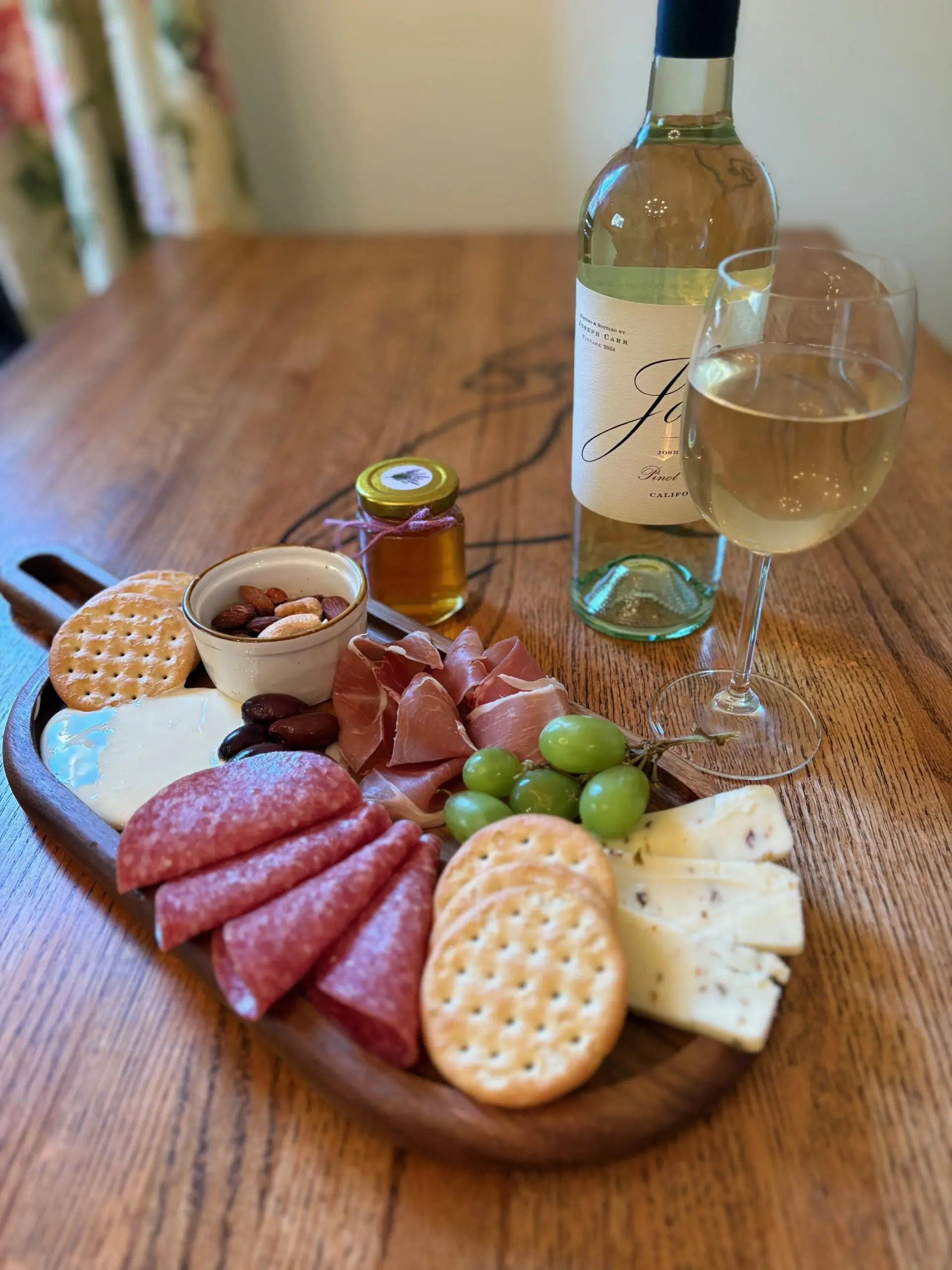 A charcuterie board with meats, cheeses, crackers, and a glass of white wine.