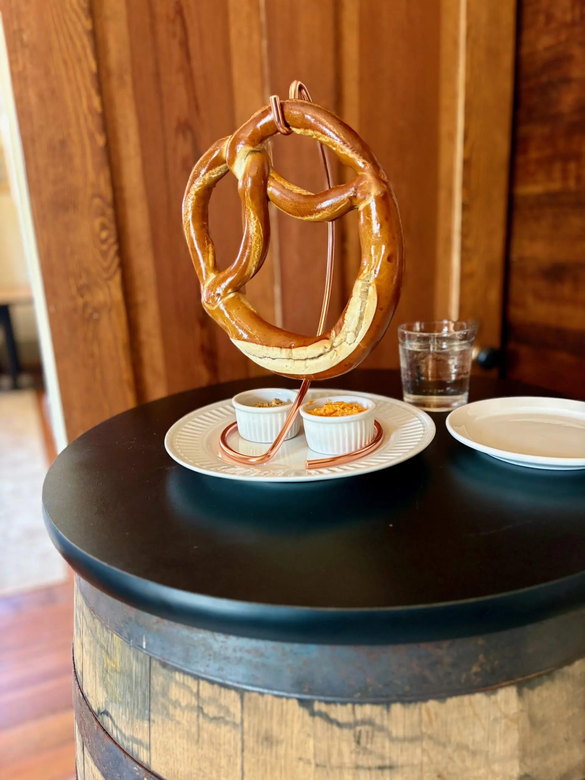 A pretzel on a stand with dipping sauces on a table.