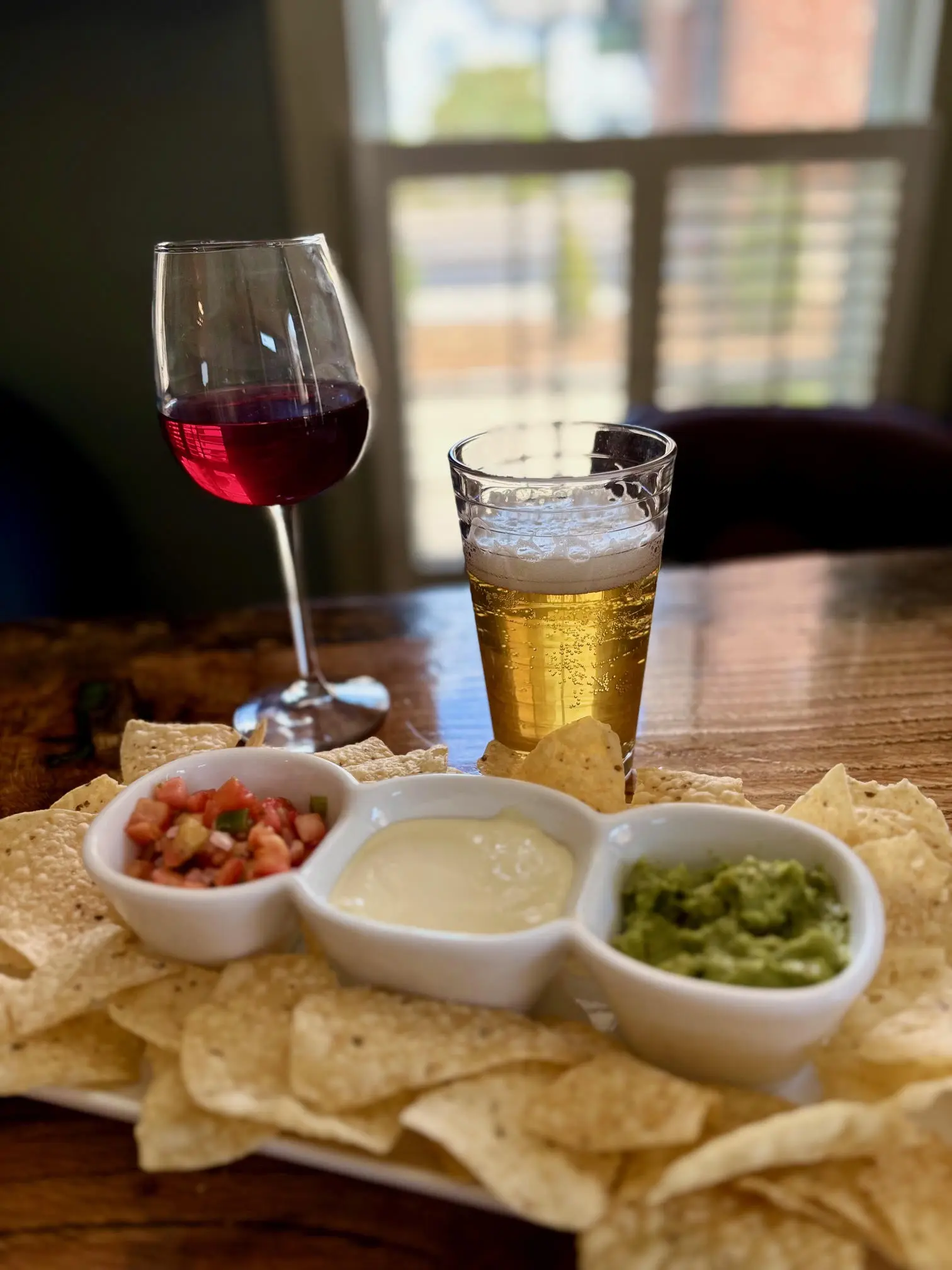 A glass of red wine, a pint of beer, and three dips on a wooden board.