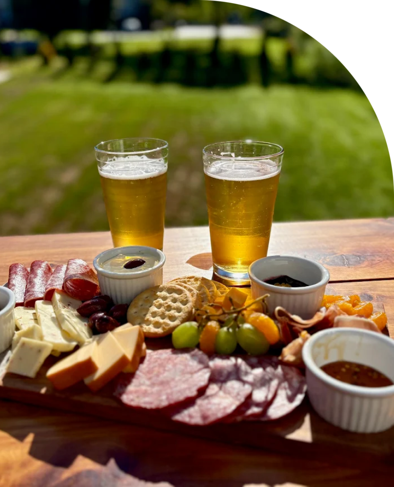 A charcuterie board with meats, cheese, and two glasses of beer.
